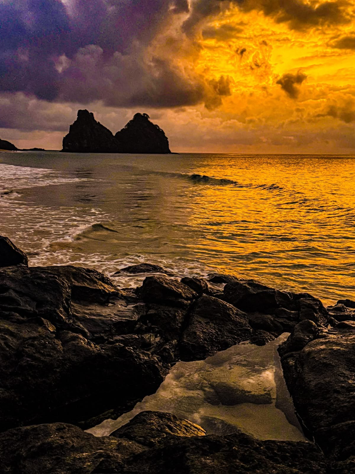 Morro Dois Irmãos em silhueta ao pôr do sol, com pedras em primeiro plano