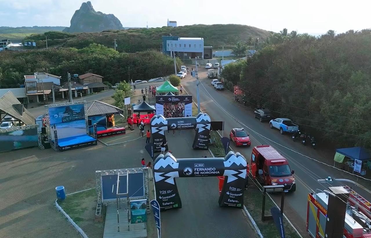 Vista aérea da arena de largada na Vila dos Remédios, com os pórticos da prova e o Morro do Pico ao fundo